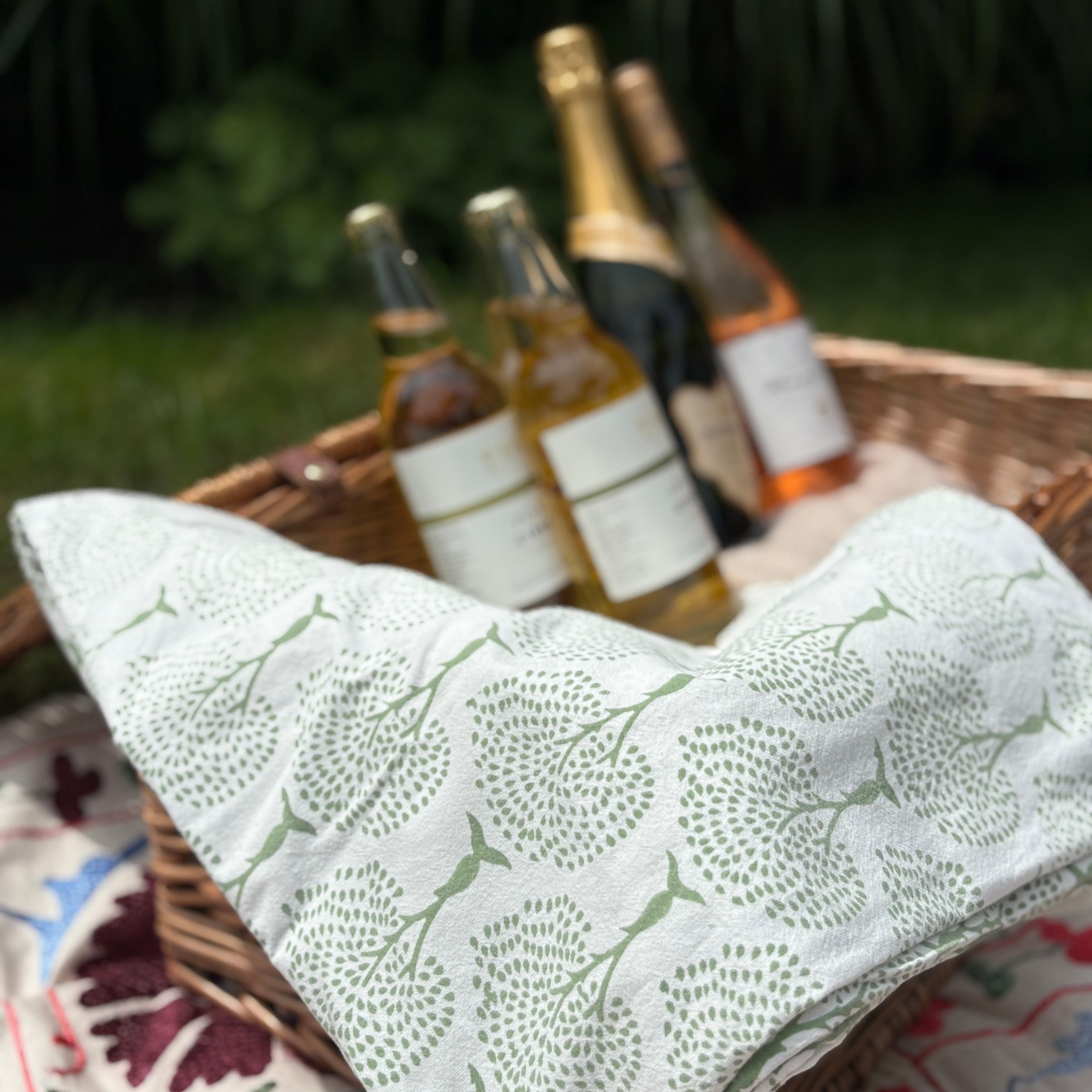 Wicker picnic basket with bottles of wine and a patterned cloth on a grassy background